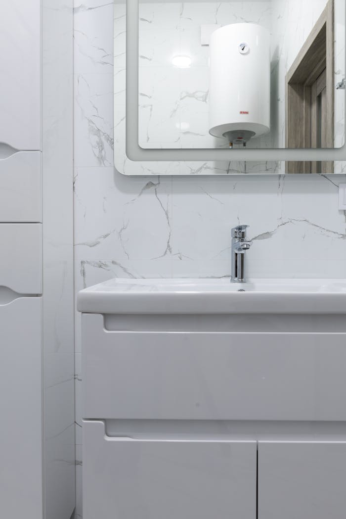 Modern bathroom interior with white washbasin and tap under mirror reflecting water heater at home